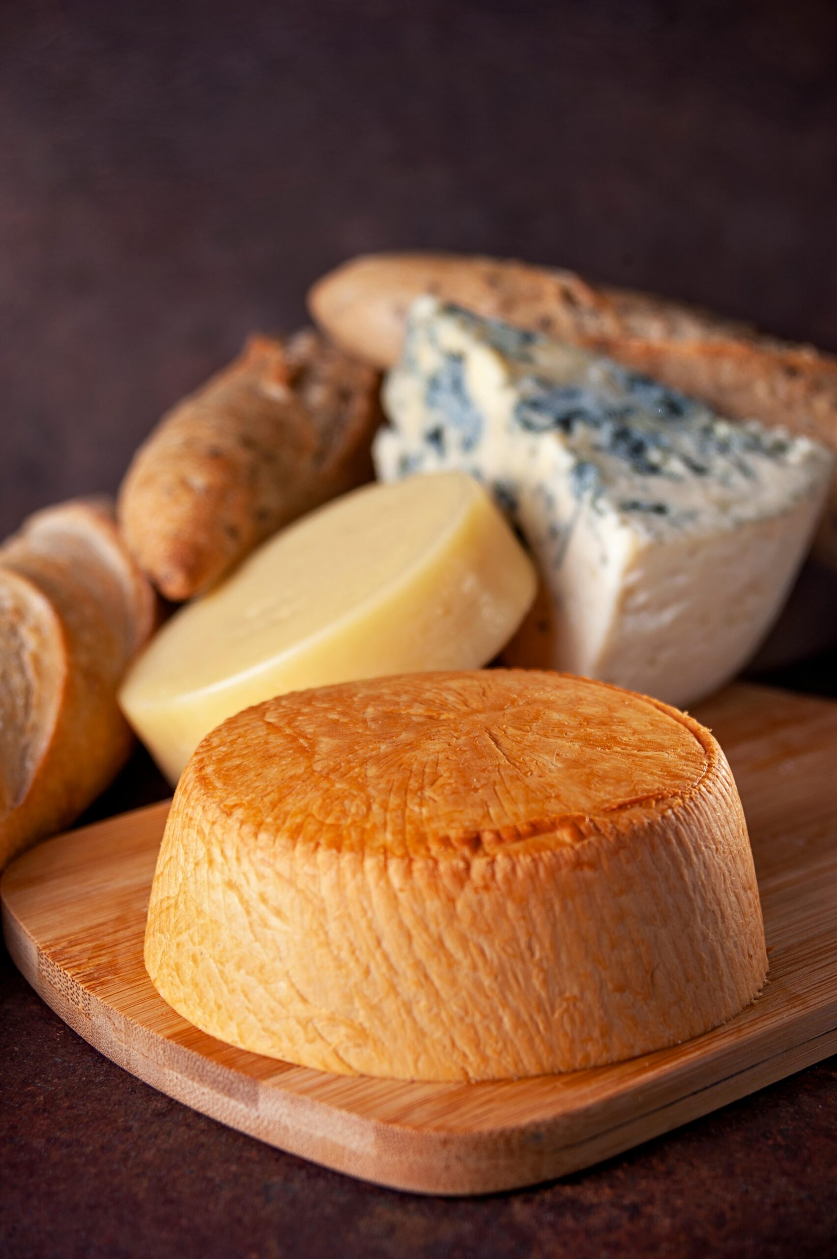 A variety of artisanal cheeses and bread displayed on a wooden board, ideal for gourmet presentations.